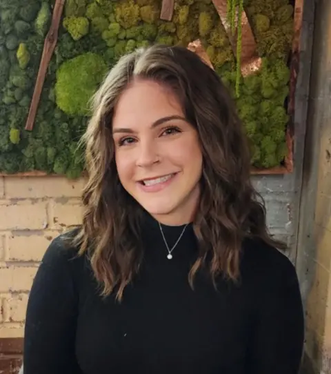 When should you turn the heating on? Olivia Carney Olivia, a 33-year-old woman, wearing a black jumper. She is smiling at the camera and is sitting in front of a white brick wall with some foliage decoration
