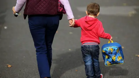 Cornwall and Isles of Scilly facing child poverty 'crisis' Brian Lawless/PA Wire A young boy wearing a red jumper and jeans is holding a woman's hand as they walk side by side. The small child is holding a blue Minions backpack in his other hand. The woman is wearing a purple jacket and jeans. She is holding keys in her other hand.