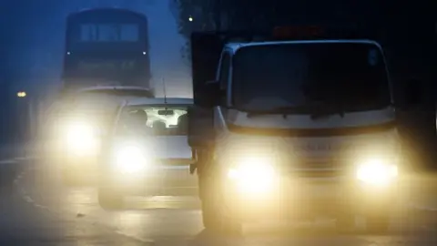 Car headlights to be reviewed after drivers complain of being 'blinded' at night EPA A truck, with two cars behind it have bright headlights in the early morning light