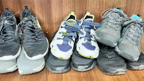 Jersey Employment Trust Six pairs of trainers are piled up in a box. There are black and grey pairs  and one with blue laces.