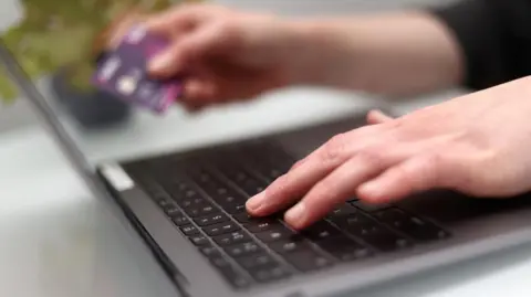 'You're willing to lose money, but not the person' PA Media A woman typing on a laptop keyboard, holding her credit card in her right hand.