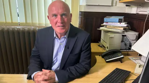 Horizon sub-postmasters call for retrial in Post Office murder case A man in a suit sits behind a desk