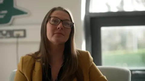 High food prices forcing parents to skip meals A woman wearing glasses and a yellow blazer looks into camera, seated on an armchair in a white office with a bright window behind her.
