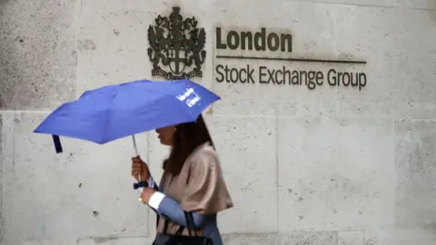 AFP via Getty Images A person carrying a blue umbrella walks past a sign reading 'London Stock Exchange Group' on the side of a brick facade, in London in 2017.