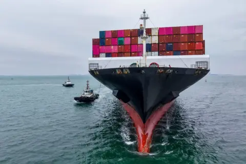 Bankers on edge, a gilded cash room and US blaming China Getty Images A large cargo ship is sailing away from the camera. It is stocked with storage containers of bright pinks, reds, greens and blues.