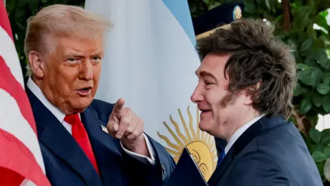 US beef prices are soaring. Will Trump's plans lower them? Reuters Two men wearing suits stand in front of the American and Argentinian flags. One man points toward the camera.