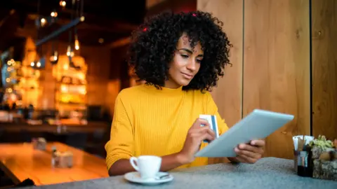 What are National Insurance and income tax and what could change in the Budget? Getty Images A woman wearing a yellow jumper holds her credit card in one hand while she looks at a tablet in a cafe.