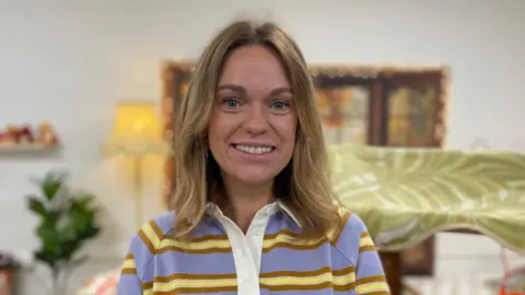 'I left Wales and moved to England for free childcare' Grace has mid-length blonde hair and is wearing a striped lilac and yellow rugby-style shirt with a white collar. She is smiling with the nursery in the background.