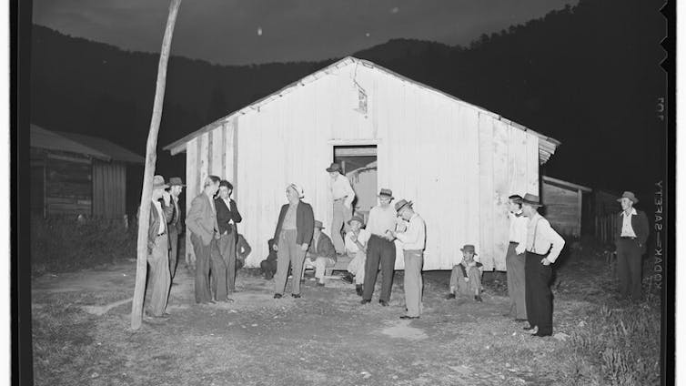 For many miners, religion and labor rights have long been connected in coal country A black and white photo of several men in slacks and shirts standing outside a small white building.