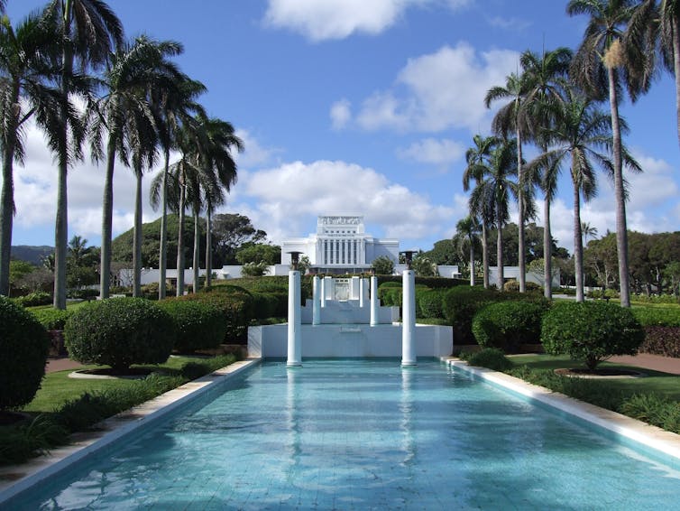 A white building in the distance, with palm trees and a clear reflecting pool in the foreground.
