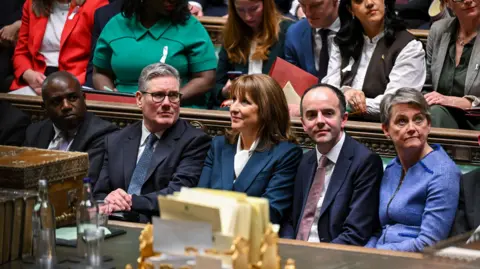 House of Commons/PA Wire The Chancellor Rachel Reeves is pictured inside the House of Commons alongside the Prime Minister and other MPs. She is sat on the green benches, looking across the room. 