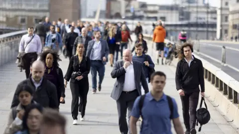 Getty Images People in suits and casual outfits walk across a bridge on a sunny day.