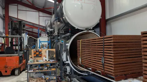Fire-blocking chemicals promise safer buildings A neat bundle of wood being moved into a large cylinder, where it will be exposed to a vacuum and pressure.
