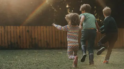 Getty Images Three children in a garden run towards a fence, with the picture taken behind them. The sun creates a rainbow-like effect.