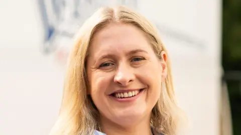 Dunsters Farm Hanna Barlow with shoulder length blonde hair wearing a blue and white striped shirt and smiling at the camera