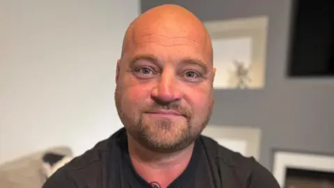 Lose weight or lose your jobs, offshore workers told Offshore worker Phil Perry, who has a bald head and is wearing a black T-shirt, is smiling at the camera. He has tattoos on arms.