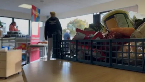 A blue plastic box, packed with various food items in the foreground, while volunteers wander around in the background waiting for parents to arrive at Okehampton primary school.