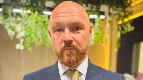 Lose weight or lose your jobs, offshore workers told Graham Skinner, a man with a beard, wearing a blue suit, white shirt and yellow/gold tie looking at camera.