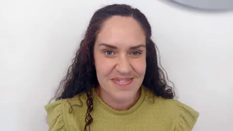 BBC A head and shoulders crop of Carla McLoughlin in a green top smiling while looking into the camera against a grey background.