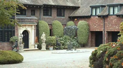 A red brick house with white portico porch, statues outside and a large gravel drive