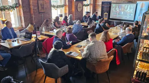 Representatives from 30 small businesses watching chancellor Rachel Reeves deliver the Budget at the Copper Rivet Distillery in Chatham, Kent. The people can be seen sat at two long tables with a camera tripod in the image.