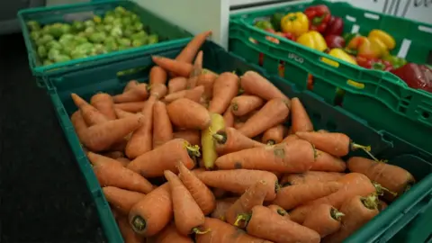 Woman volunteers at the Blackpool foodbank that helped her Three green food crates with sprouts, carrots and yellow and red peppers