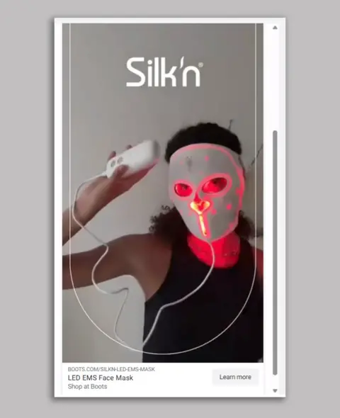 Silk'n A Silk'n advert showing a woman in a black tank top with dark curly hair wearing a white LED face mask and holding the controller while it beams red light on to her face