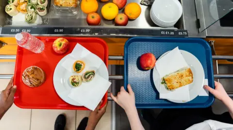 Getty Images Two children holding food trays in a canteen. 
