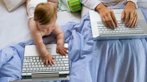 Getty Images A baby and woman both place their hands on two laptops 