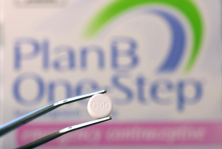 A pair of tweezers holds a white pill, photographed in front of a box that says 'PlanB One Step.'