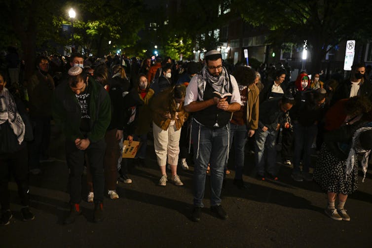 Young men and women stand in rows outside at night, some of them bent forward in prayer.