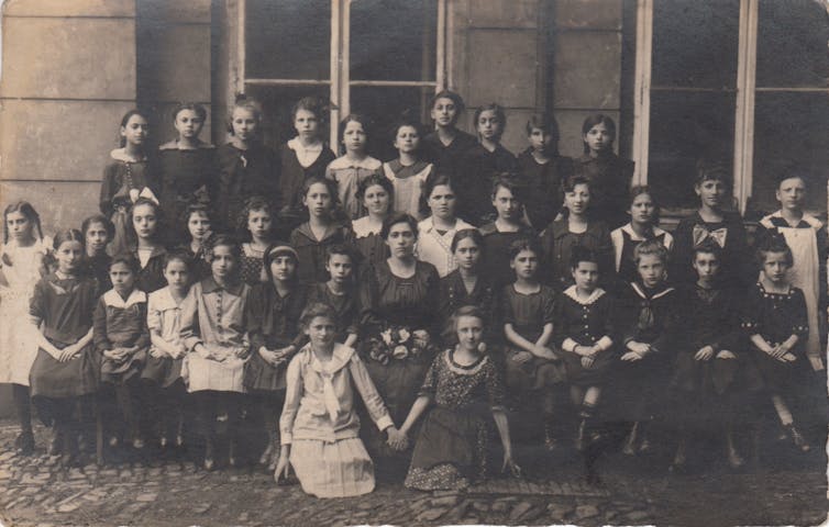 A black and white photo shows several rows of girls formally posed for a large class picture outside.