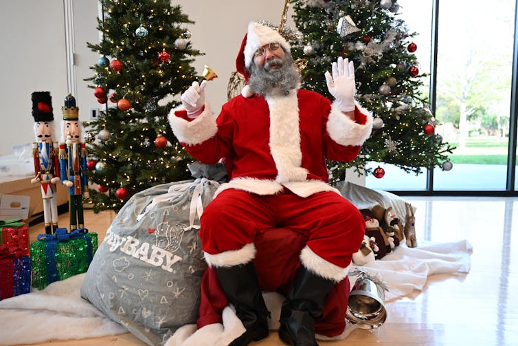 A man dressed as Santa in a gray beard smiles festively.