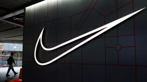 Reuters A shopper walks past a Nike store with a large lit-up version of the company's logo on the side.