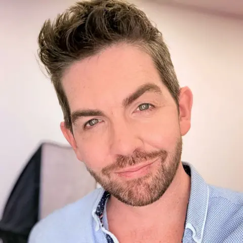 Scott McGlynn A man with short brown hair, in a blue shirt, smiles at the camera