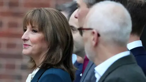 Getty Images A profile close-up photo of Rachel Reeves, dressed in a dark green suit jacket and white blouse, with members of her Treasury ministry team out of focus
