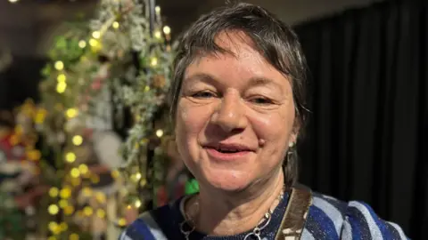 Woman with short dark hair smiling at the camera. There is twinkly lights behind her 