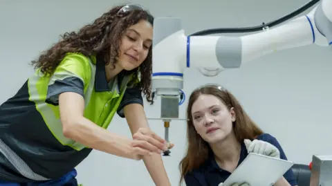 Getty Images Female engineers performing collaborative robotic operation training in smart factory one controlling robotic machine other observing process teamwork focus in hands-on automation skill lab