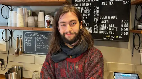 A man in a red shirt standing in a coffee shop.