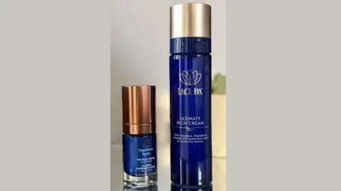 Victoria Woollaston Two deep blue bottles of facial cream - one small by Augustinus Bader, one by Lacura - are stood on a table
