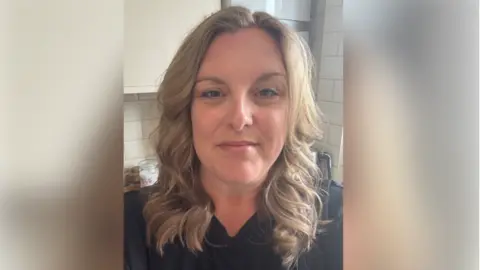 Jade Hunter Jade Hunter, a woman who is standing in a kitchen which has white tiles. She is wearing a black T-shirt and is looking directly at the camera and smiling.