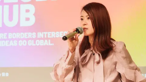 Moeko Suzuki Moeko Suzuki, co-founder of Startup Lady, speaking into a microphone at a public event
