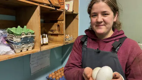 Beth Mellish holds duck eggs, with shelves of honey, cards and eggs beside her.