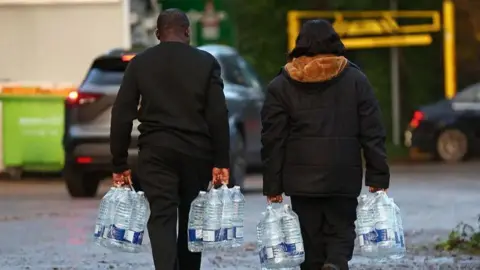 Getty Images Two people with backs to camera walking along with bottles of water in both hands