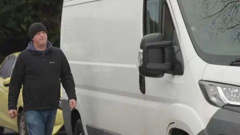 'Throw the parcel at the back door' Dave wearing a black beanie and coat walks up to the door of his white van.