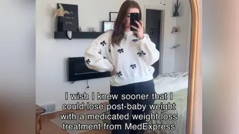 MedExpress A woman looks in the mirror holding her phone, with text saying 'I wish I knew sooner that I could lose post-baby weight with a medicated weight loss treatment from MedExpress'