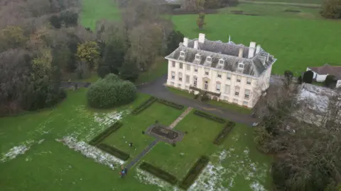 Croda and the story of Lorenzo's oil as firm marks centenary A drone view of a large stately home, a cream-coloured rectangular building with a grey roof and four rows of windows, set in formal gardens surrounded by green trees.