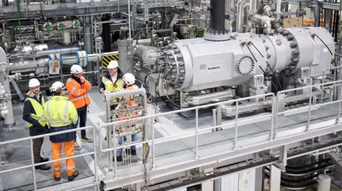 Everllence Five men in hi-viz jackets talk while standing next to heat pump machinery.