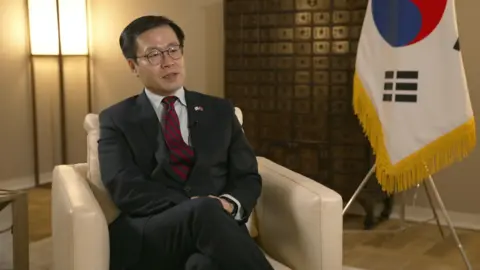 UK and South Korea strike trade deal South Korea's trade minister Yeo Han-koo sits in a cream leather chair with his country's flag in the background as he is interviewed by a BBC reporter.