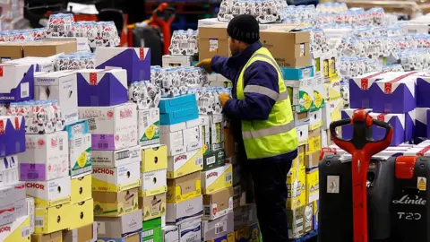 Getty Images A worker wearing a hi-vis jacket stacks shelves in a supermarket warehouse. 